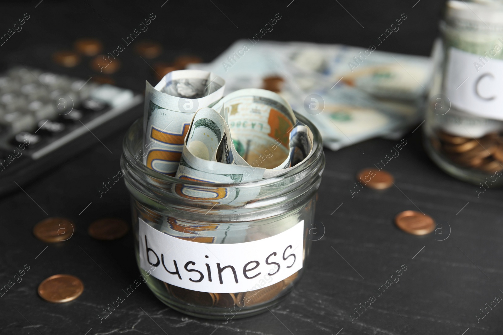 Photo of Glass jar with money and tag BUSINESS on black table