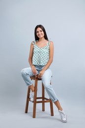 Photo of Beautiful young woman sitting on stool against light grey background