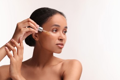 Beautiful woman applying serum onto her face on white background. Space for text