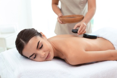 Photo of Beautiful young woman getting hot stone massage in spa salon