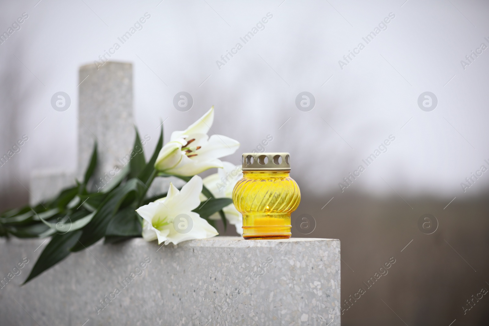Photo of White lilies and candle on light grey granite tombstone outdoors. Funeral ceremony