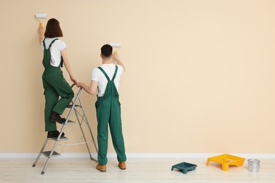 Photo of Young workers painting wall with rollers indoors, space for text. Room renovation