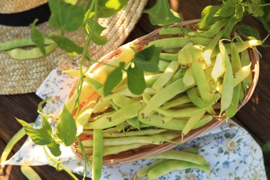 Photo of Wicker basket with fresh green beans on wooden table in garden, top view