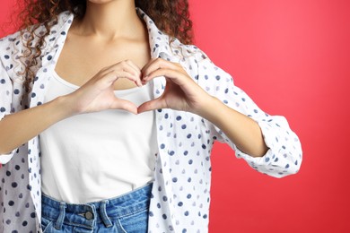 African-American woman making heart with hands on red background, closeup