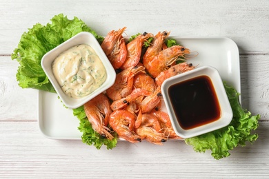 Plate with juicy shrimps and sauces on table, top view