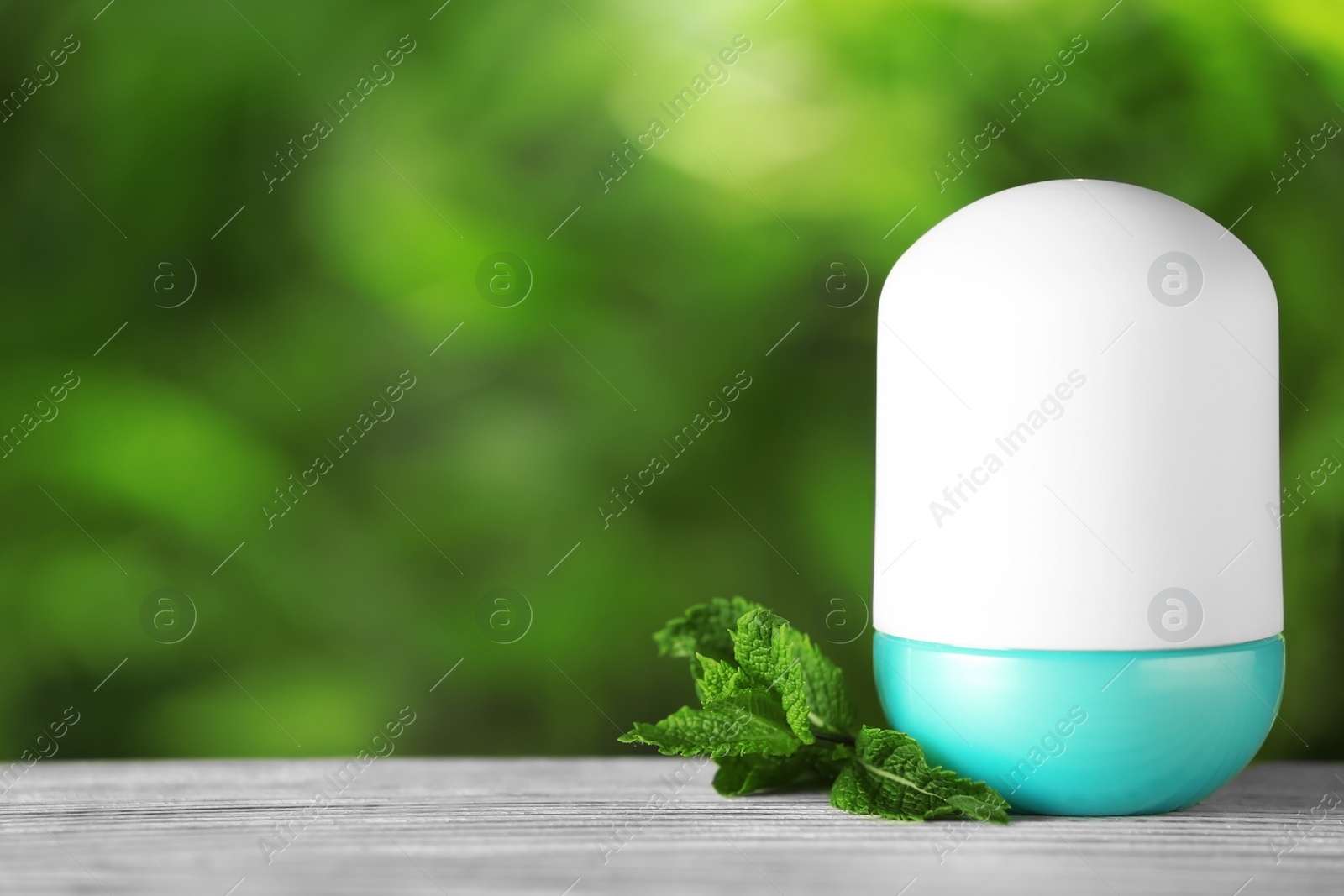 Photo of Natural roll-on deodorant with mint on wooden table against blurred green background. Space for text