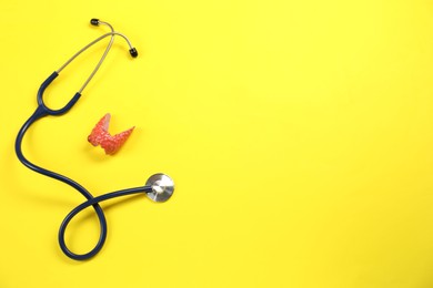 Endocrinology. Stethoscope and model of thyroid gland on yellow background, top view. Space for text