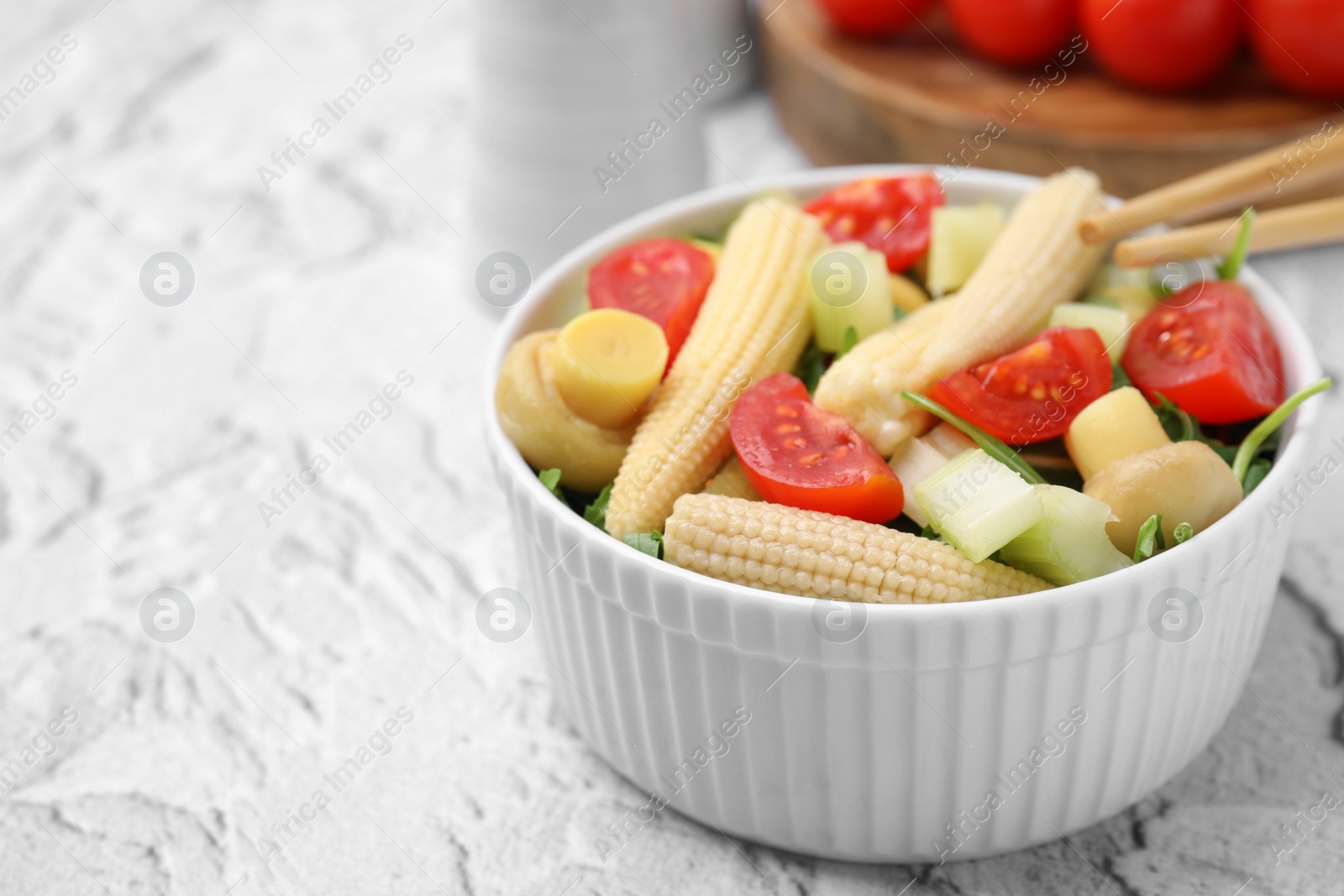 Photo of Tasty baby corn with vegetables and champignons on grey textured table, closeup. Space for text