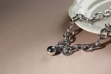 Metal chain with pendant on light brown background, space for text. Luxury jewelry