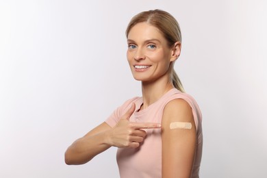 Photo of Smiling woman pointing at adhesive bandage on arm after vaccination on light background