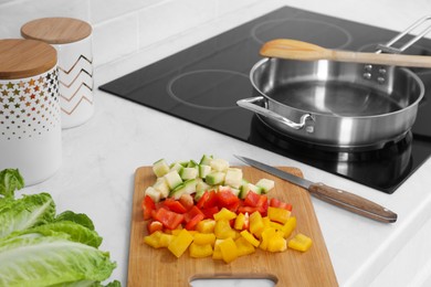 Wooden board with cut vegetables and knife near saute pan in kitchen