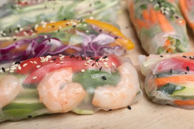 Photo of Delicious rolls wrapped in rice paper on wooden board, closeup