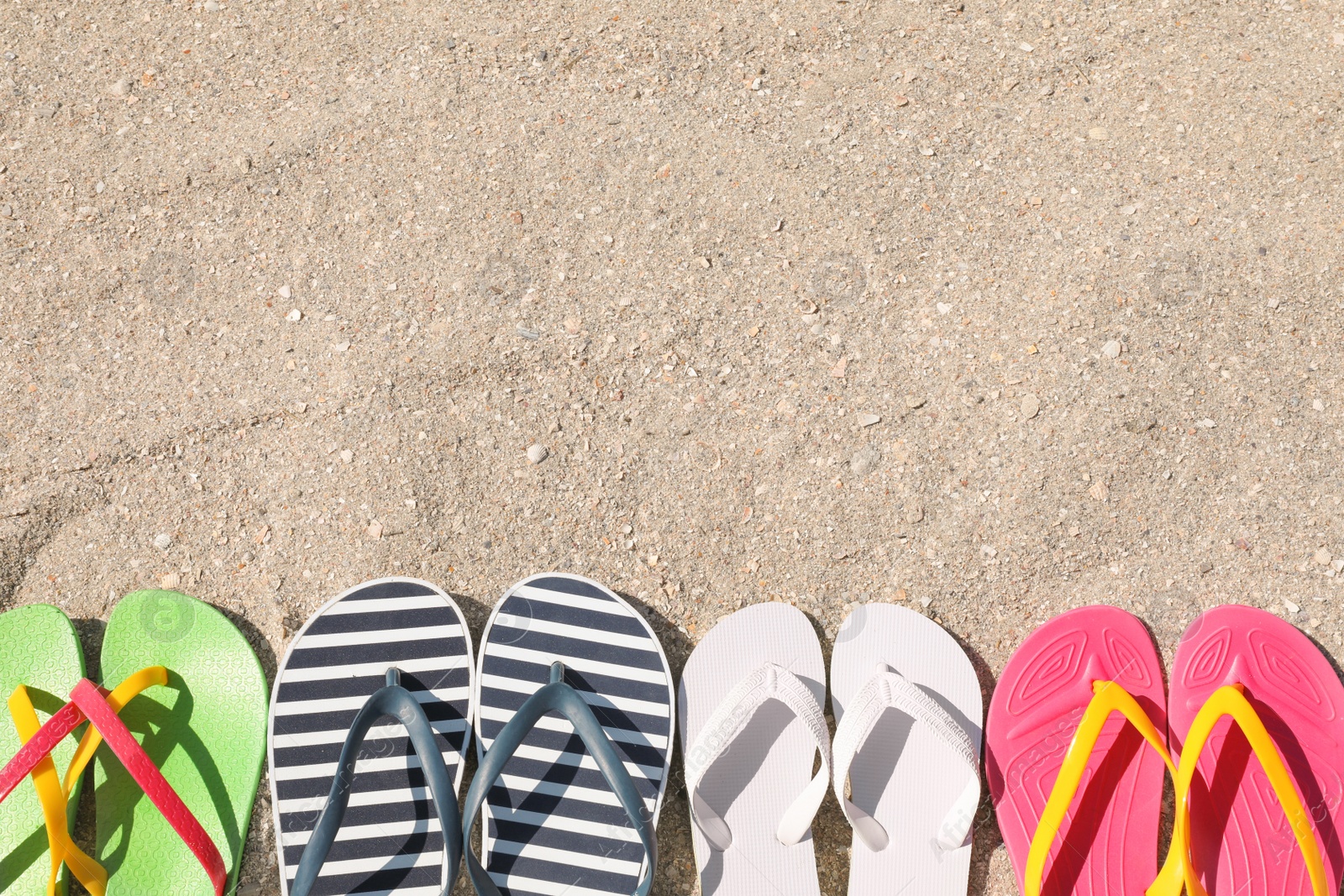 Photo of Many different flip flops on sand, flat lay. Space for text