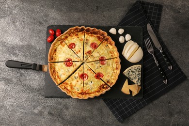 Photo of Delicious homemade cheese quiche, ingredients and cutlery on gray table, flat lay