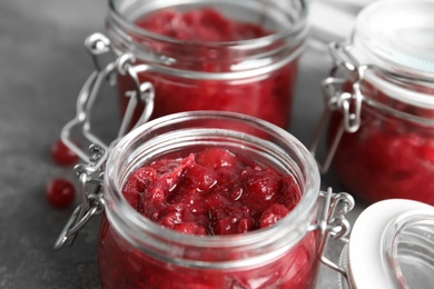 Photo of Glass jars with tasty cranberry sauce on table, closeup