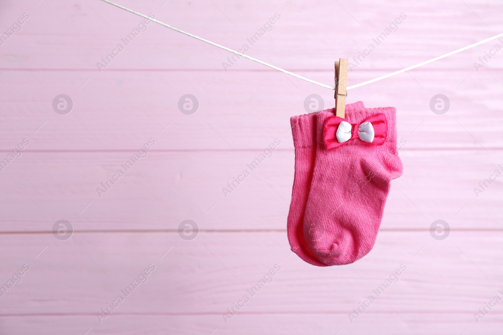 Photo of Pair of socks on laundry line against pink wooden background, space for text. Baby accessories