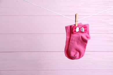 Photo of Pair of socks on laundry line against pink wooden background, space for text. Baby accessories