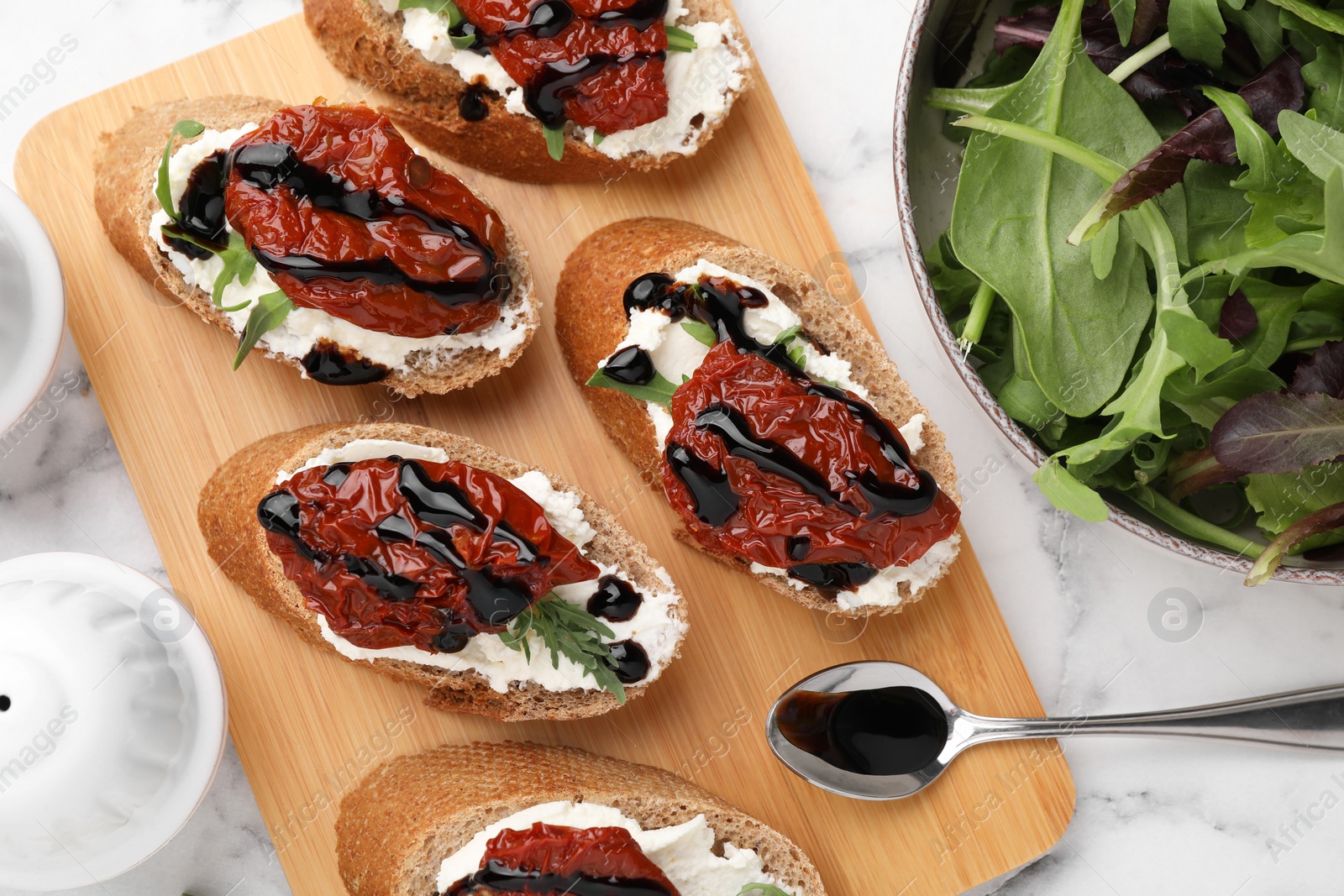 Photo of Delicious bruschettas with sun-dried tomatoes, cream cheese, balsamic vinegar and ingredients on white marble table, flat lay