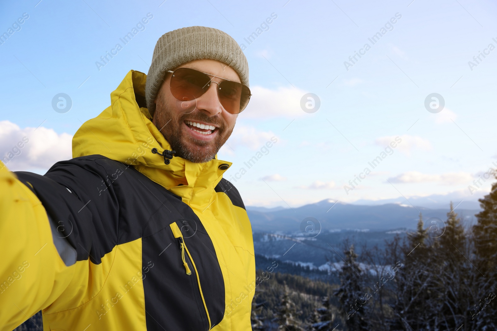 Image of Smiling man in sunglasses taking selfie in mountains