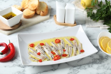 Photo of Tasty pickled anchovies with spices and products on white marble table