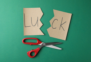 Photo of Cut paper with word LUCK and scissors on green background, flat lay