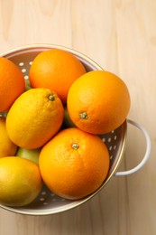 Colander with fresh citrus fruits on wooden table, top view