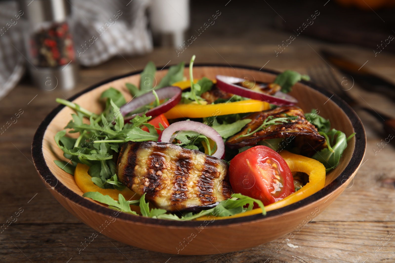 Photo of Delicious salad with roasted eggplant and arugula served on wooden table