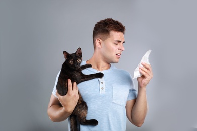 Photo of Young man with cat suffering from allergy on grey background