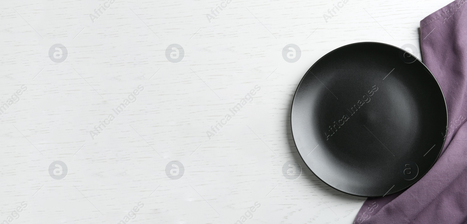 Photo of Black plate and fabric on white wooden table, flat lay. Space for text