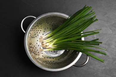 Fresh green spring onions in colander on black table, top view