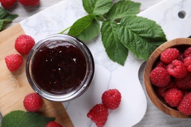 Photo of Delicious raspberry jam, fresh berries and green leaves on table, flat lay
