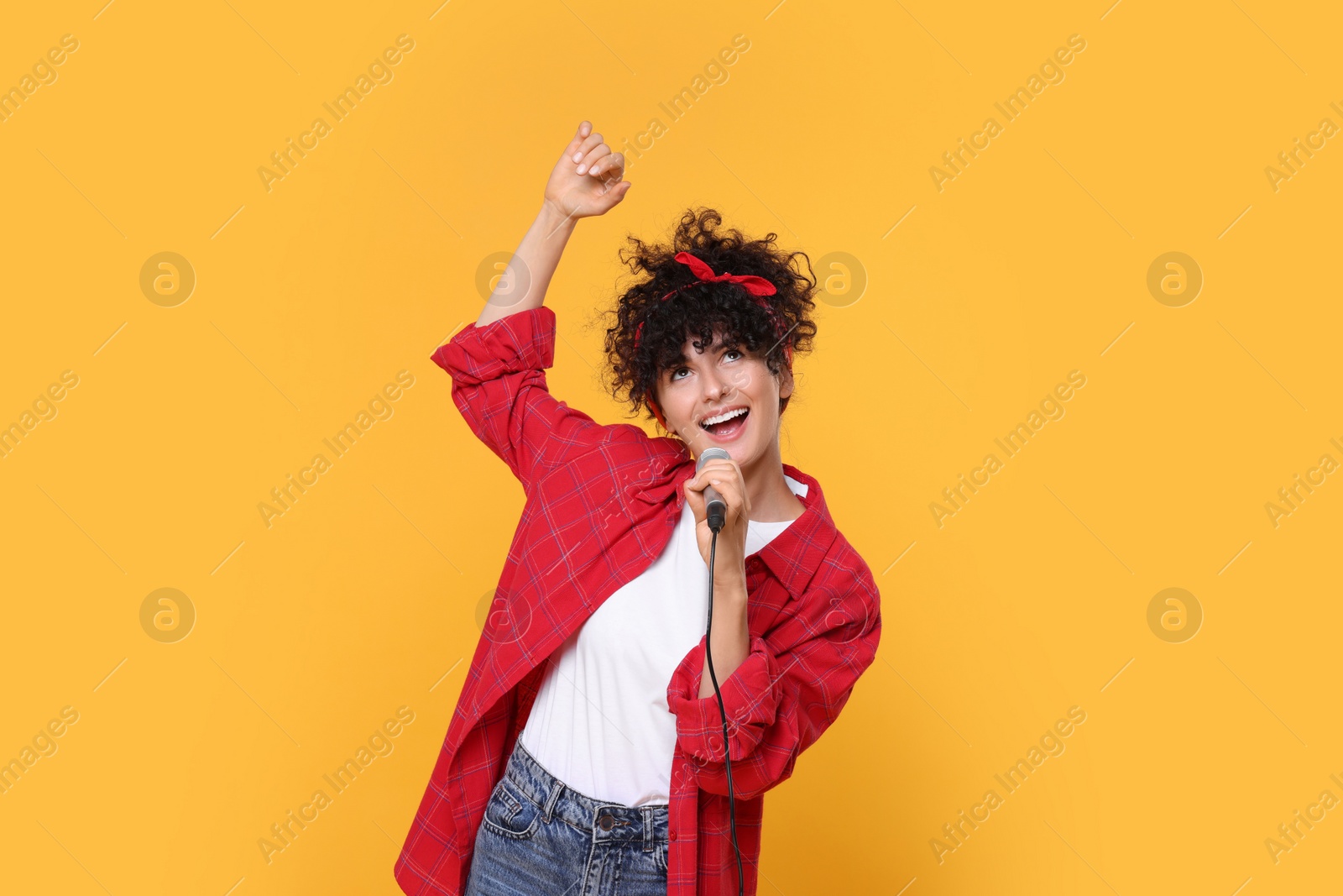 Photo of Beautiful young woman with microphone singing on yellow background