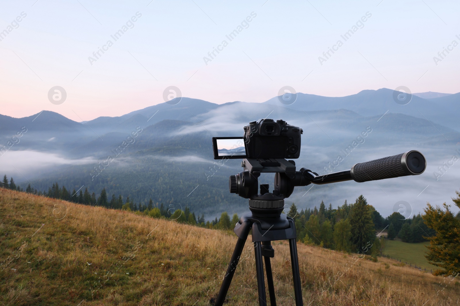 Photo of Tripod with modern camera in mountains. Space for text