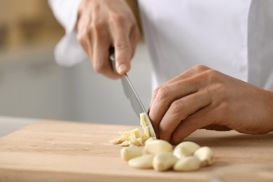 Photo of Professional chef cutting garlic at table indoors, closeup