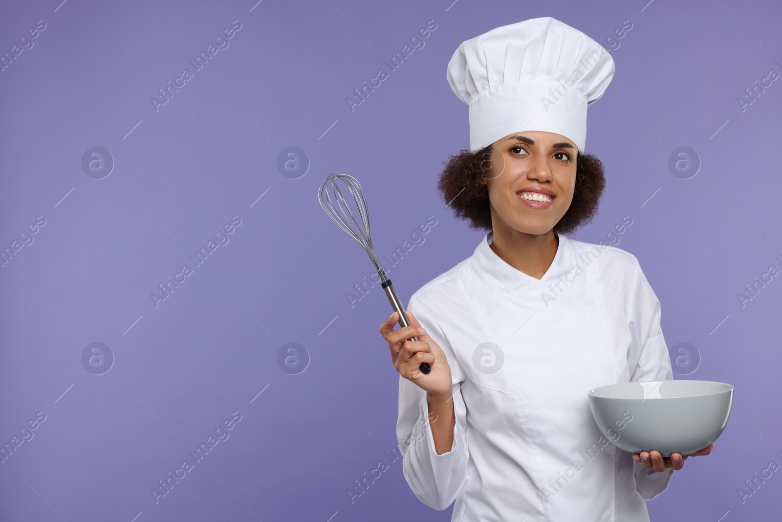 Photo of Happy female chef in uniform with whisk and bowl on purple background. Space for text