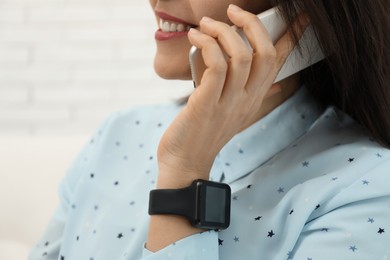 Mature woman with smart watch talking on phone indoors, closeup