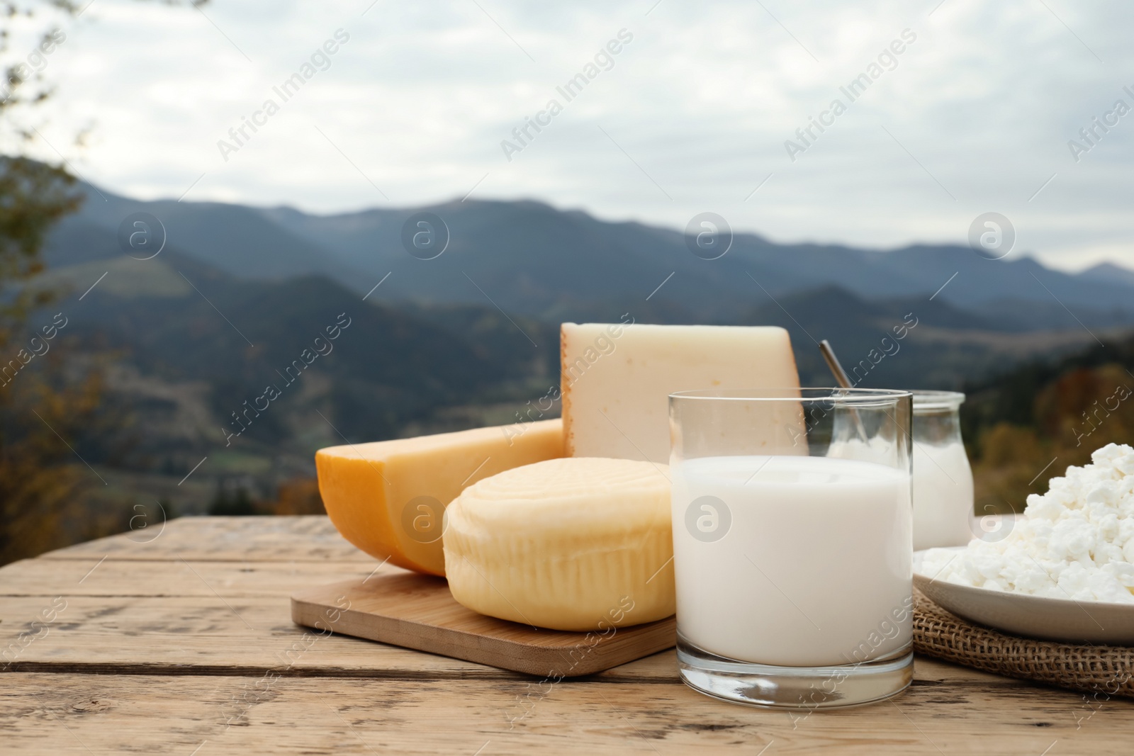 Photo of Tasty cottage cheese and other fresh dairy products on wooden table in mountains