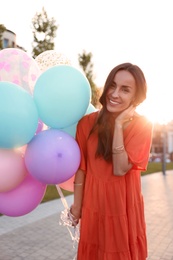 Cheerful young woman with color balloons outdoors on sunny day