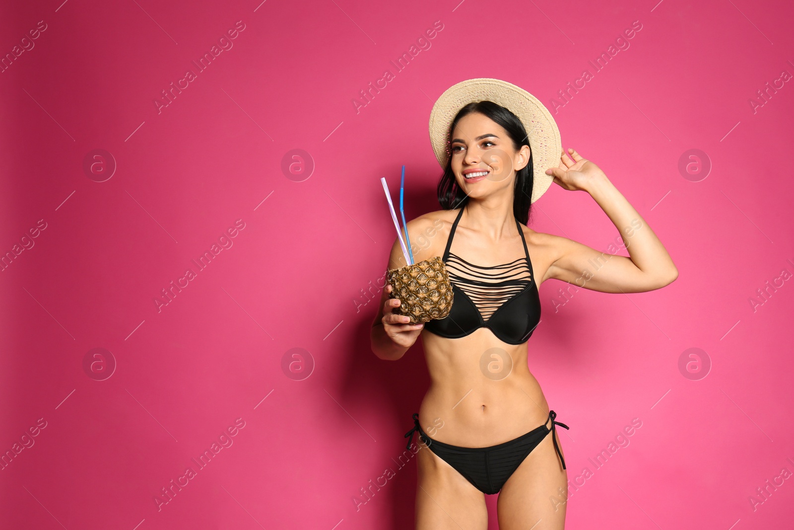 Photo of Beautiful young woman in black bikini with cocktail on pink background. Space for text