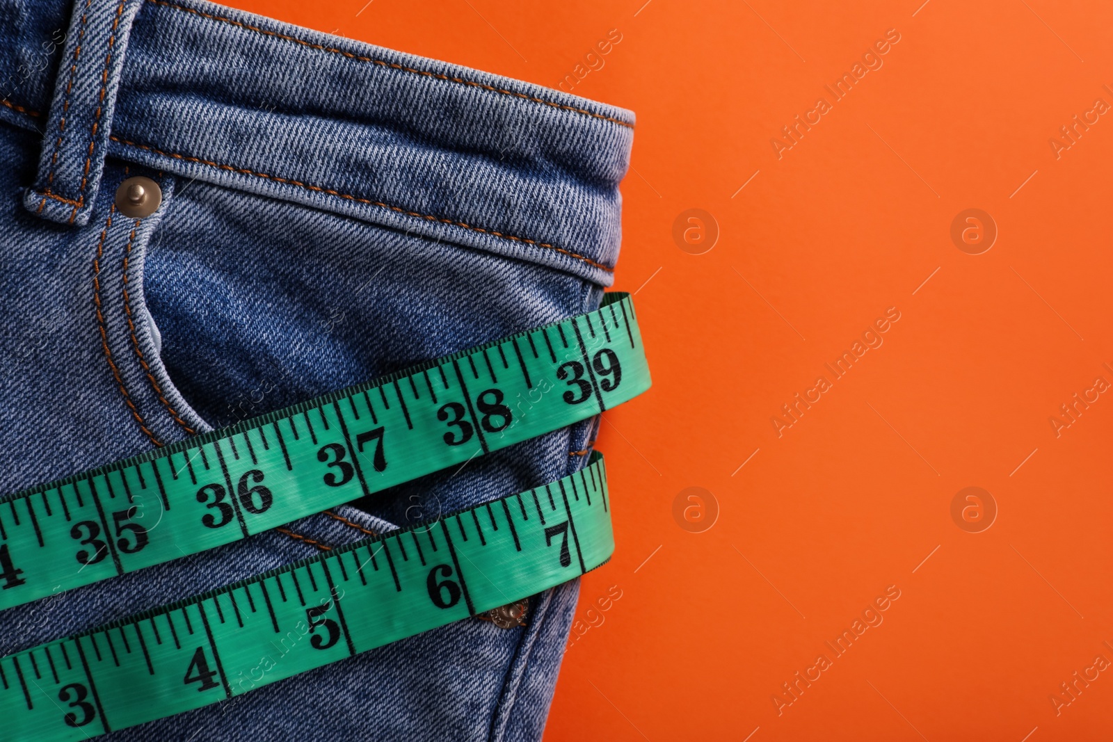 Photo of Jeans and measuring tape on orange background, top view with space for text. Weight loss concept