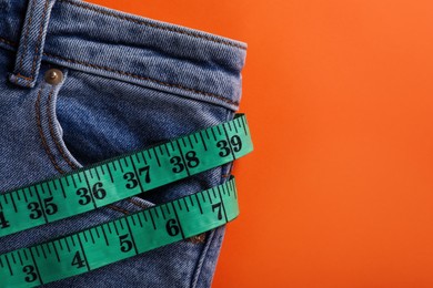 Jeans and measuring tape on orange background, top view with space for text. Weight loss concept