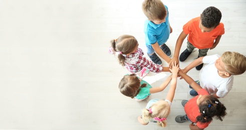 Photo of Little children putting their hands together indoors, top view. Unity concept
