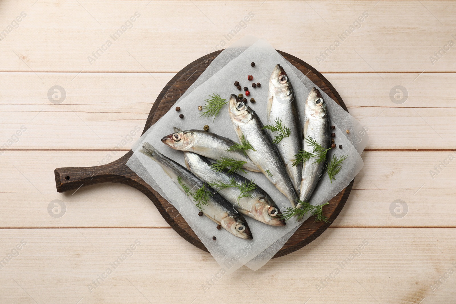 Photo of Fresh raw sprats, dill and peppercorns on light wooden table, top view