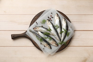 Fresh raw sprats, dill and peppercorns on light wooden table, top view