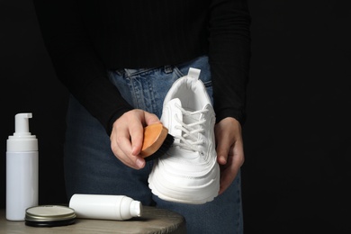 Photo of Woman cleaning stylish footwear at table against black background, closeup. Shoe care accessories