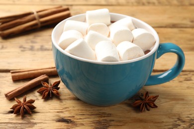 Photo of Tasty hot chocolate with marshmallows and spices on wooden table, closeup