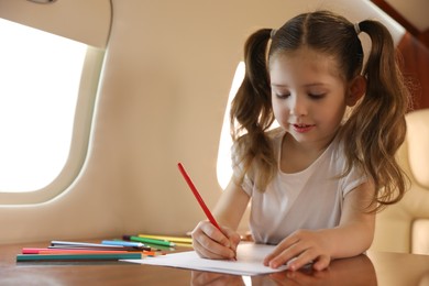 Photo of Cute little girl drawing at table in airplane during flight