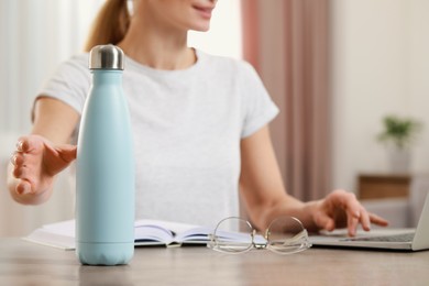 Woman taking thermo bottle indoors, closeup view
