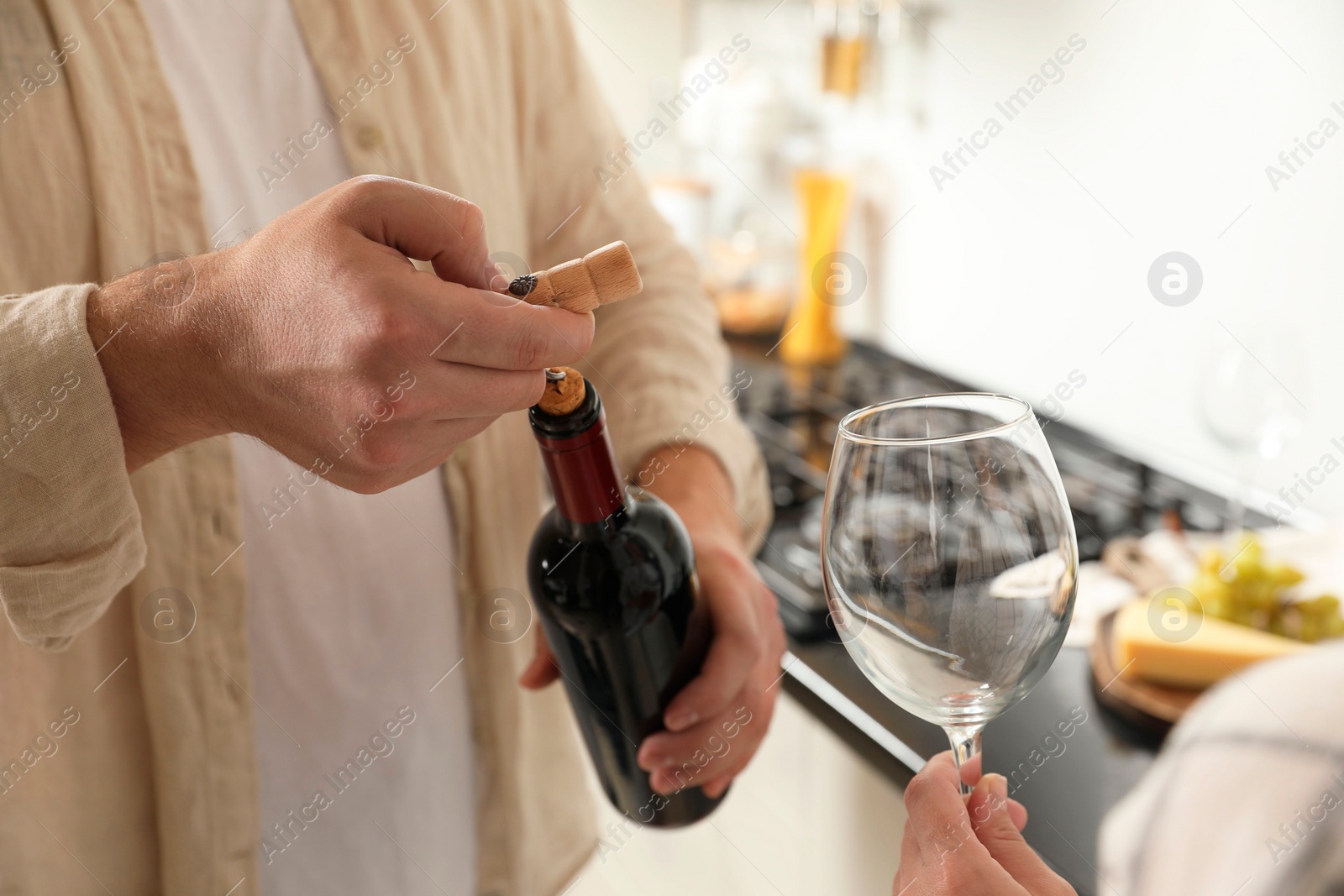 Photo of Man opening wine bottle with corkscrew while woman holding wineglass indoors, closeup