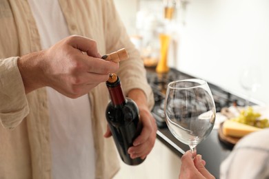 Man opening wine bottle with corkscrew while woman holding wineglass indoors, closeup